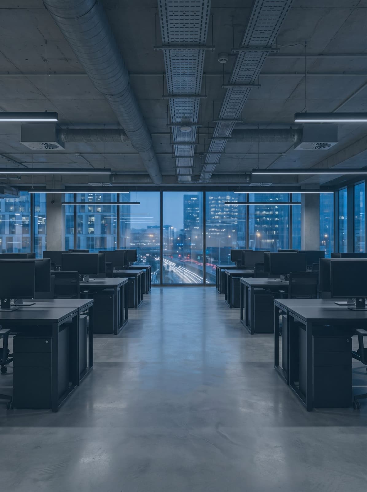 Rows of empty desks and monitors either side of a walkway in an open-plan office